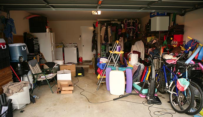 Cluttered garage filled with boxes, bicycles, chairs and assorted household items