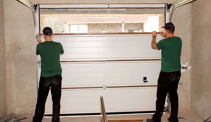 Two professionals replacing a white sectional garage door on a residential property